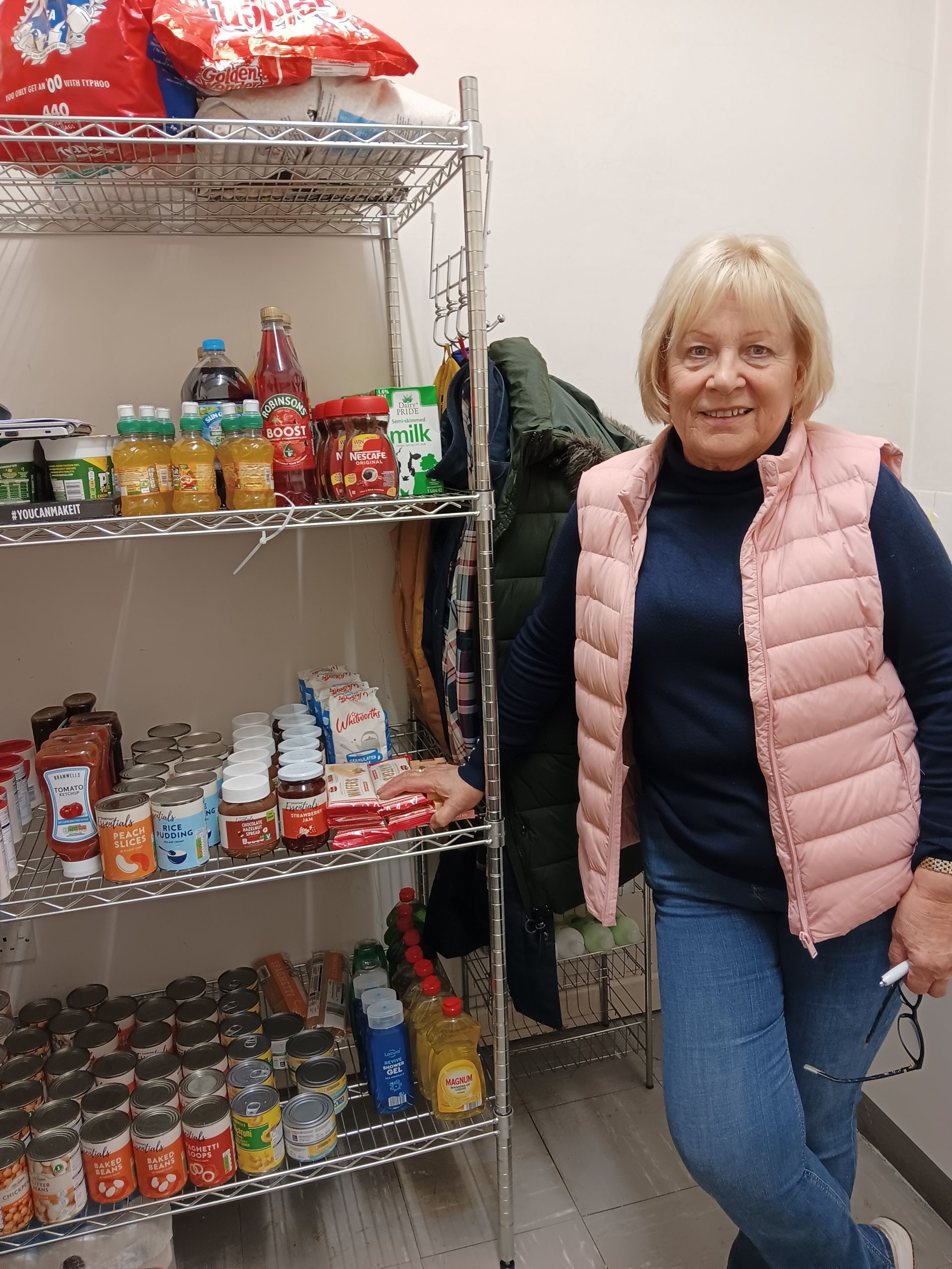 Largs Food Hub Volunteer standing next to stocked shelves