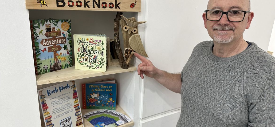 Friends of Lochshore volunteer at community book nook bookshelf with handcarved owl