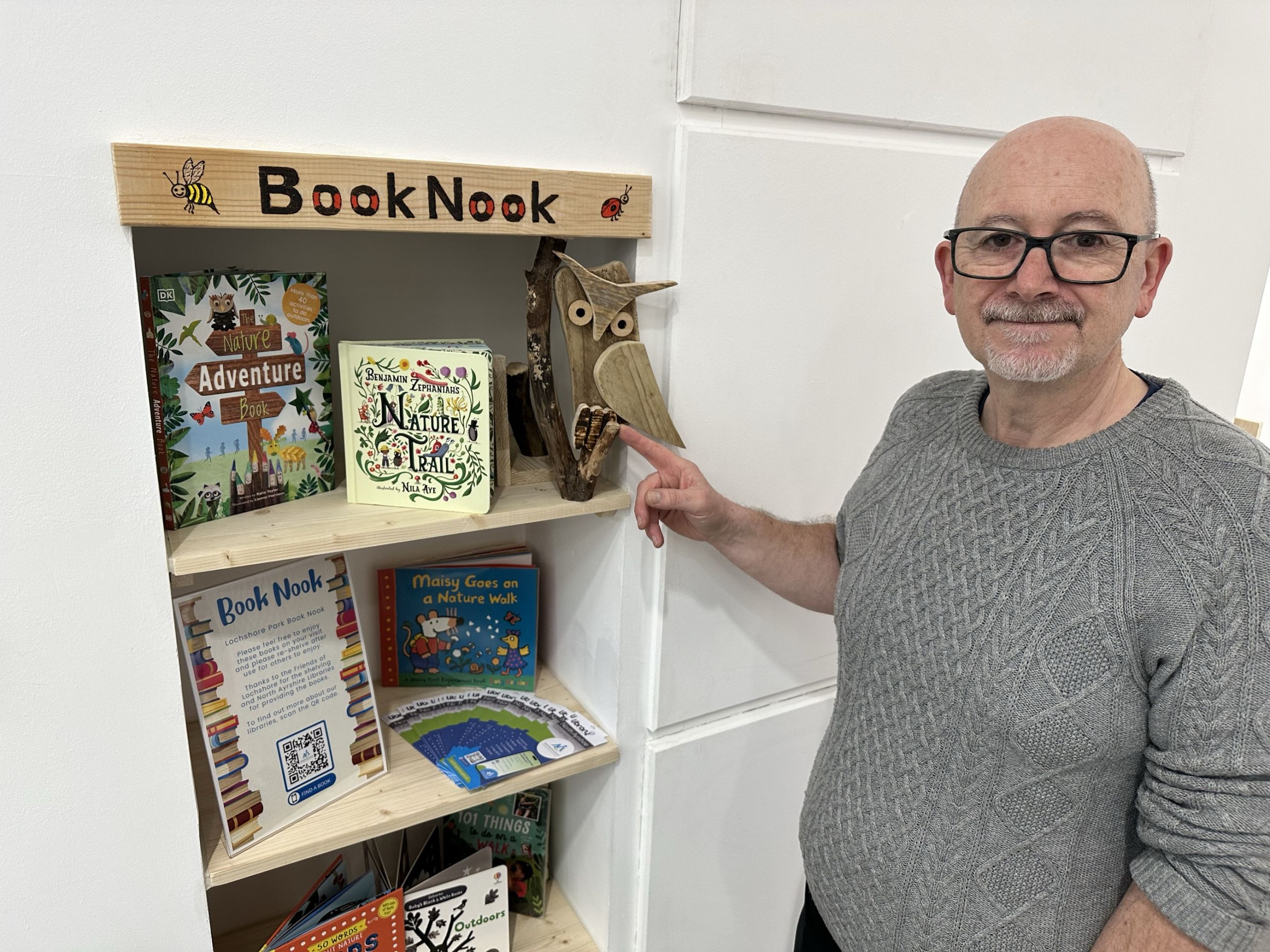 Friends of Lochshore volunteer at community book nook bookshelf with handcarved owl