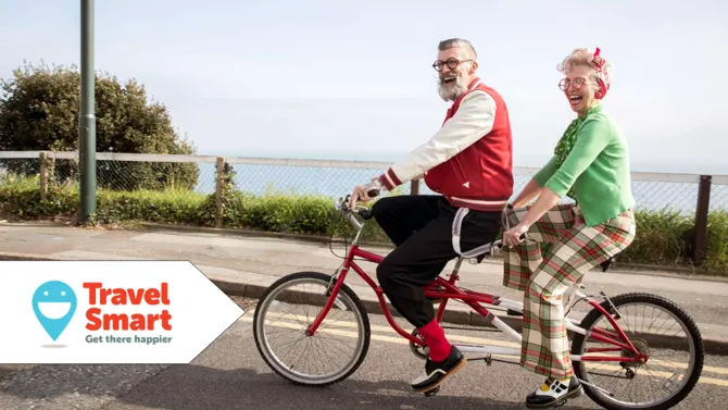 Couple in vintage clothing cycling on red bike at beachfront