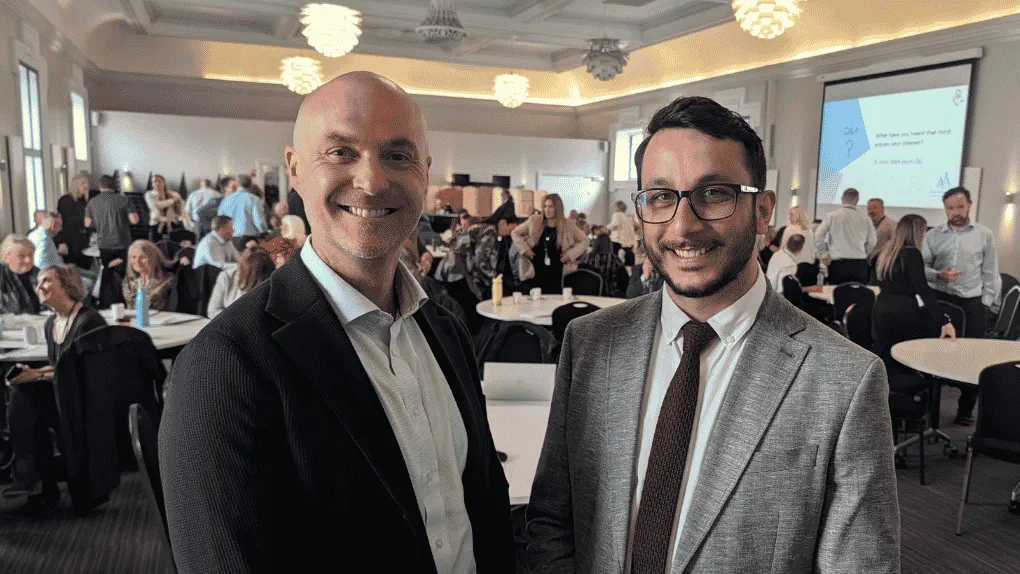 Two men standing smiling in a crowded hall