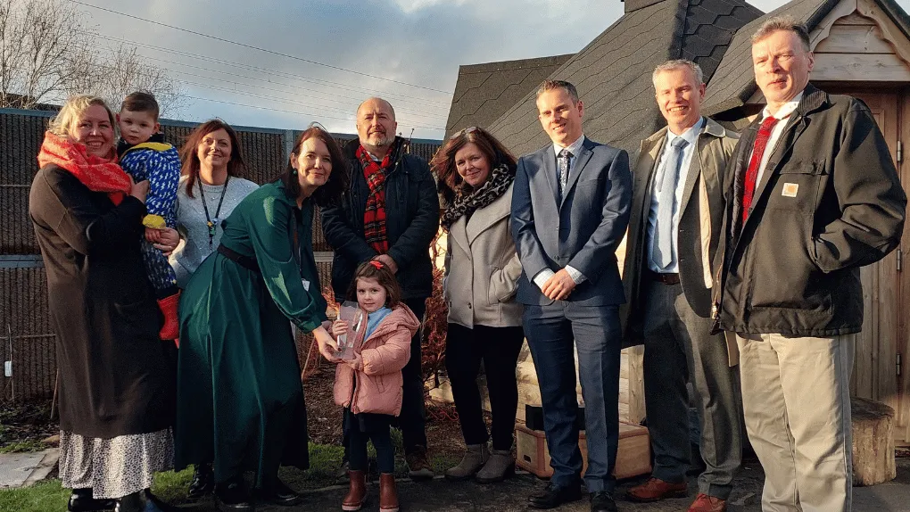 Adults and children standing in a row in front of a wooden playhouse