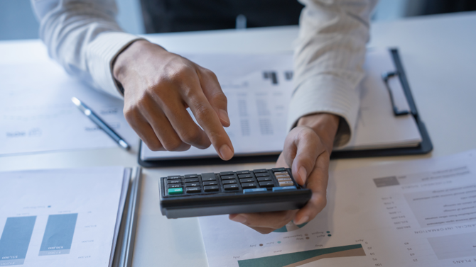 Person at desk with paperwork using calculator
