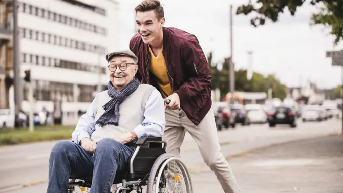 Boy pushing man in wheelchair smiling