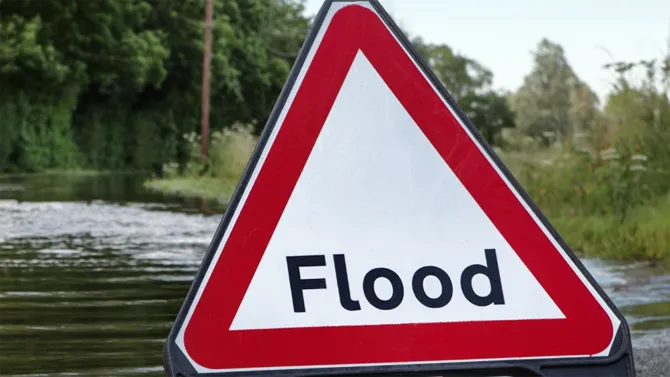 Warning sign with the word flood on it with a flooded road behind