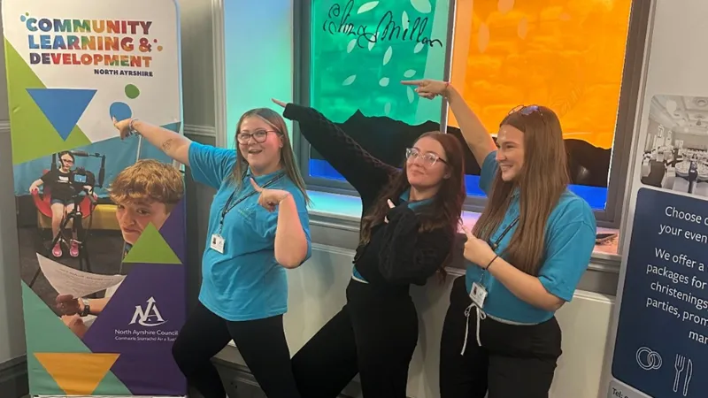 Three North Ayrshire Youth Joint Cabinet members pointing to a community learning and development banner